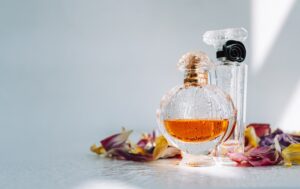 Perfume bottles with fresh water drops on white background with dried colorful flowers petals.